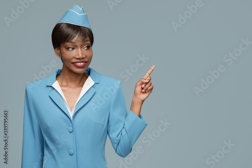 Cheerful young african stewardess points a finger at copyspace. Blue background. photo