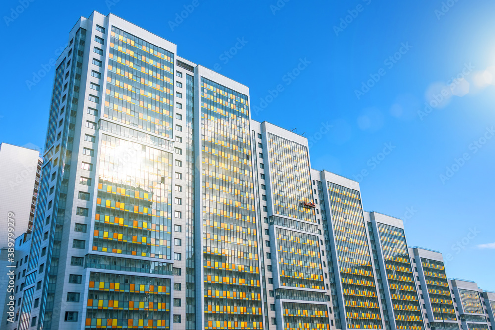 Multi-storey residential complex with sun glare, and a construction cradle by workers for finishing the external facade.