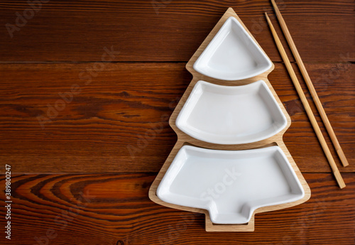 top view of empty ceramic white dish shaped like christmas tree on wooden table, three-section appetizer plate with chinese bamboo sticks, copy space
