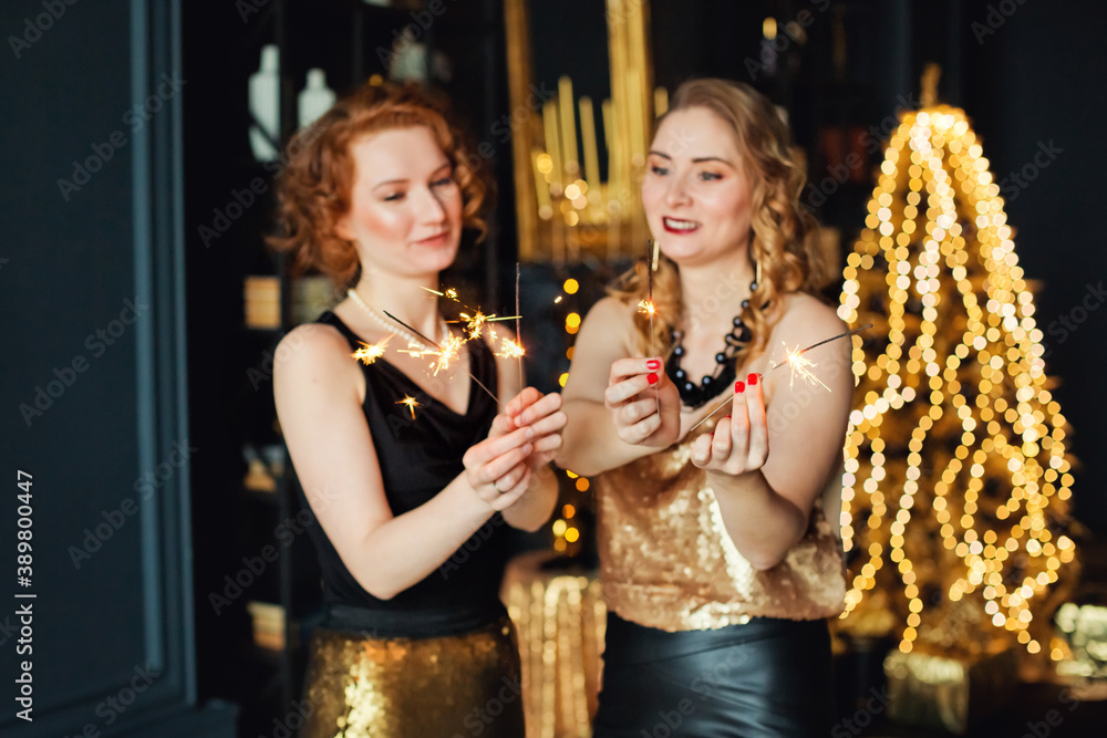 Selective focus. Sparklers in the hands of two beautiful bokeh woman Christmas garlands and gifts. Gold Christmas decoration. Happy New Year.