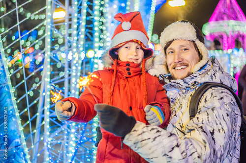 Little boy and his father with sparklers near giant fir tree and Christmas illumination on Christmas market. Xmas holidays on fair
