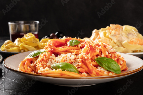 Pasta with tomato sauce, basil and Parmesan, a close-up in a restaurant with other blurred food and wine in the dark background, selective focus