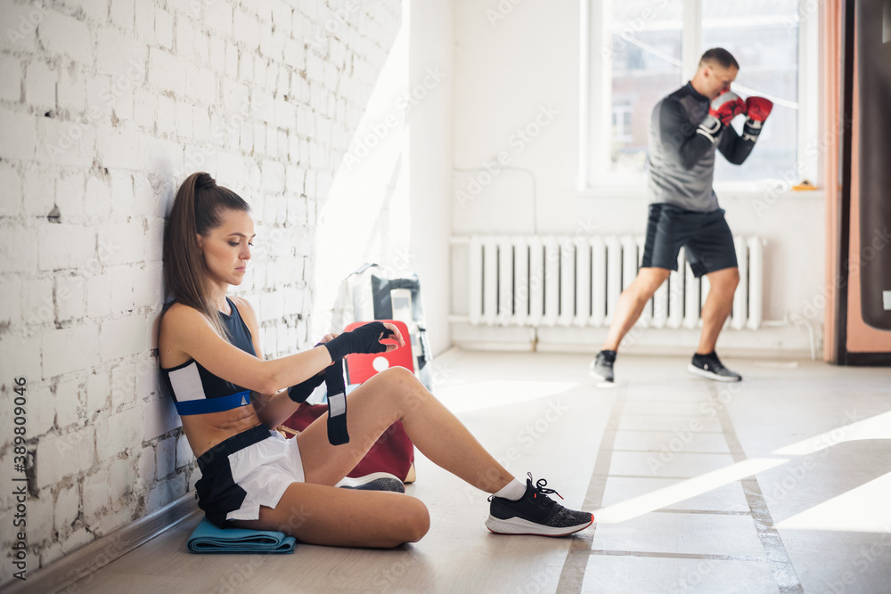 A girl boxer against a white brick wall wraps a sports bandage for boxing on her hands