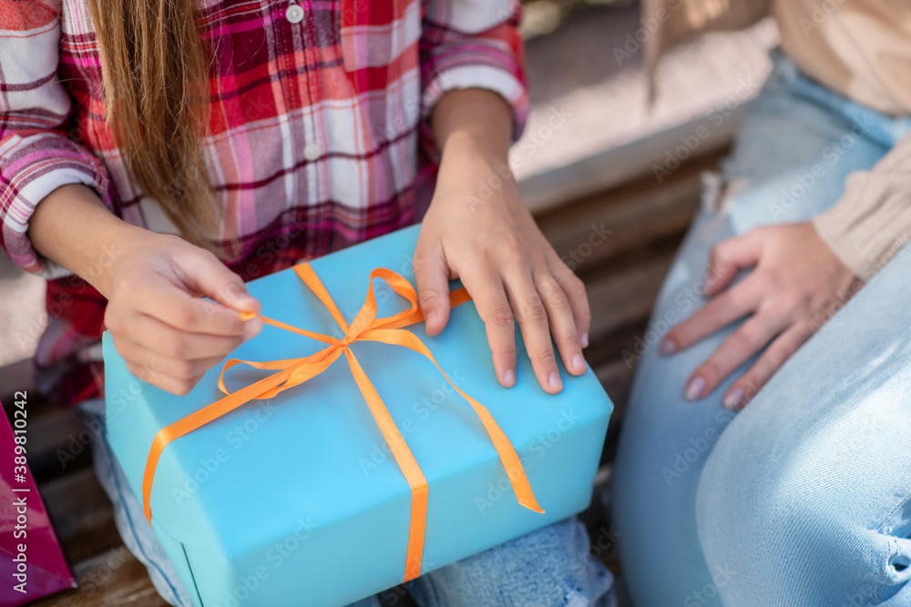 Close-up of girl hands opening present box on park bench