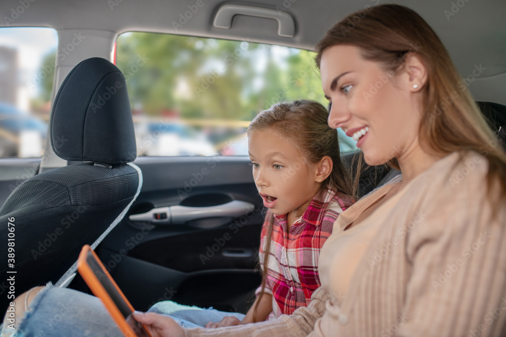 Surprised daughter and her mom checking something on tablet on backseat of car