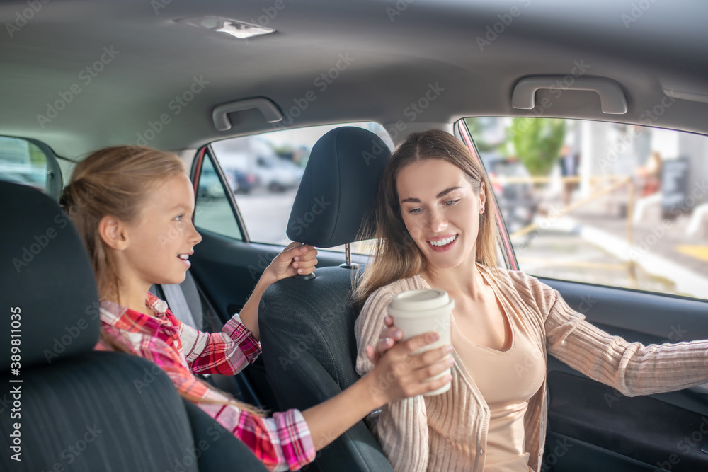 Girl giving coffee cup to her mom sitting at the wheel