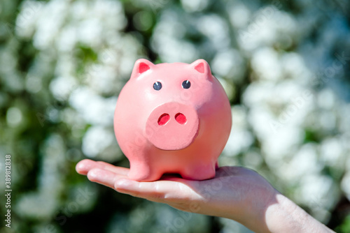 Girl holding piggy Bank against the background of blossoming spirea 