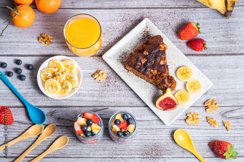 Gran desayuno al completo, con chia, pastel de chocolate con nueces y plátanos decorados con copos de avena, zumo de naranja, fresas y nueces