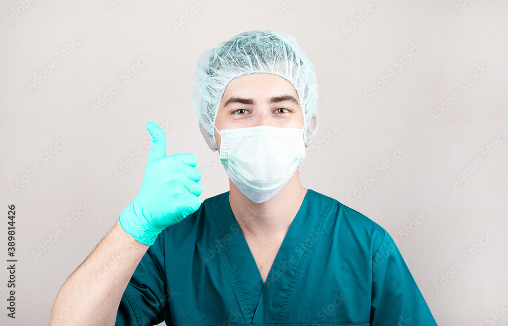 Close up of american male doctor or surgeon rise up his finger in protective facial mask over grey background Close up of american male doctor or surgeon rise up his finger in protective facial mask over grey background