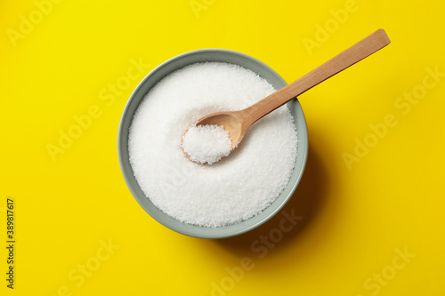 Bowl with salt and spoon on yellow background