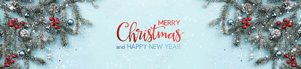 Merry Christmas and Happy New Year text on blue background with fir branches, red and silver decoration, snowflakes, pine cones, bokeh, light. Xmas greeting card. Flat lay, top view, banner