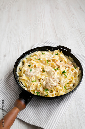 Homemade Chicken Fettuccine Alfredo in a cast-iron pan on a white wooden background, low angle view. Copy space.