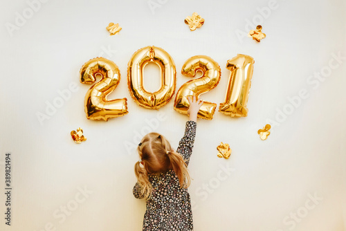 Little girl decorates the wall of the house with golden numbers 2021. Preparing the house for Christmas and New Year. photo