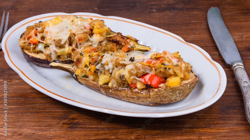 Eggplant baked with vegetables and cheese on an oval plate on a wooden table with cutlery Eggplant baked with vegetables and cheese on an oval plate on a wooden table with cutlery