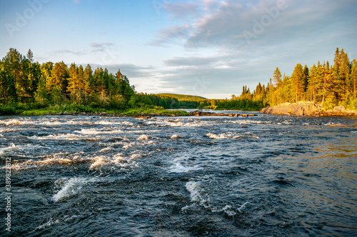 Fast rapids river against the backdrop of a forest lit at sunset