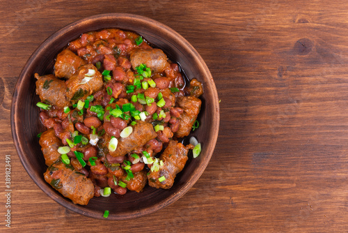 Traditional country Texas cowboy dish, beef sausages with beans in tomato sauce in a rustic clay plate on a wooden table, copy space
