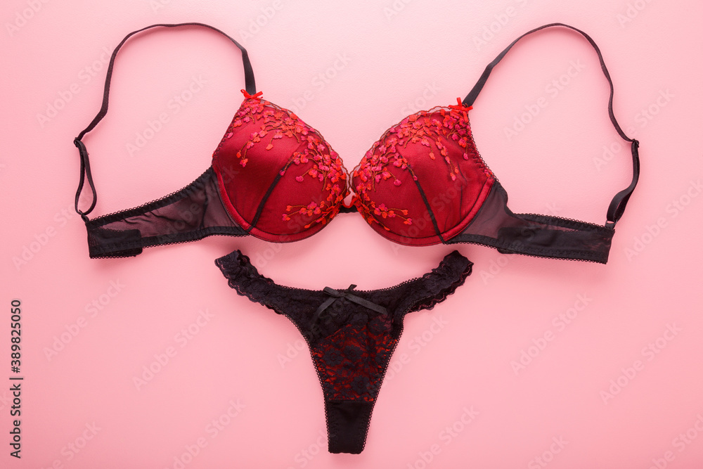 Female black red bra and string panties on light pink table background. Pastel color. Daily underwear. Closeup. Top down view. - obrazy, fototapety, plakaty 