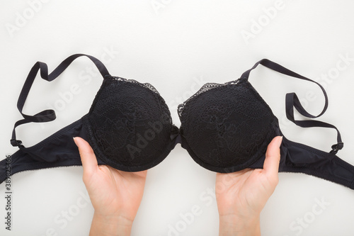 Young adult woman hands holding black bra on light gray table background. Daily underwear. Closeup. Point of view shot. Top down view.