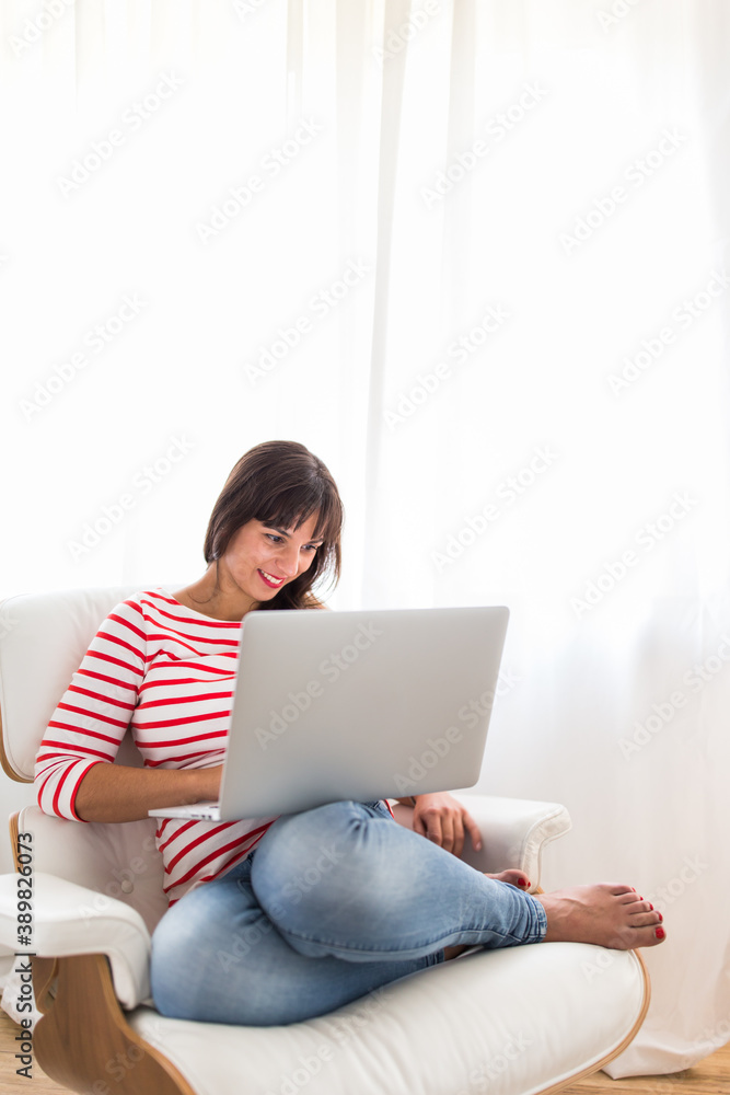 Successful young business woman sitting in a designer chair, working from home. Portrait of happy entrepreneur working on a laptop computer. Doing business remotely from the comfort of her home. Successful young business woman sitting in a designer chair, working from home. Portrait of happy entrepreneur working on a laptop computer. Doing business remotely from the comfort of her home.