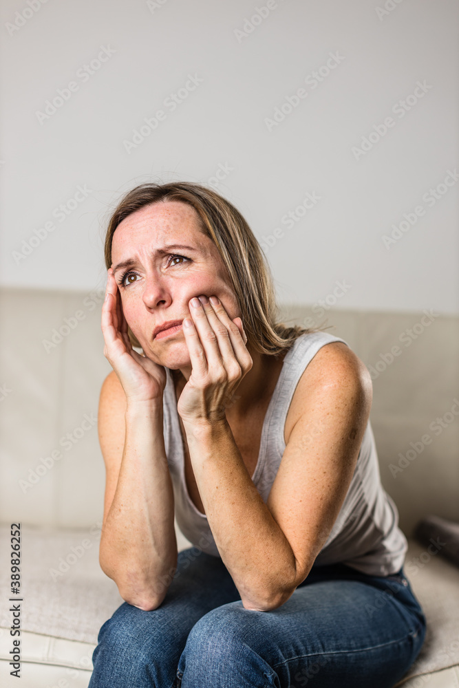 Mid-aged woman touching her cheek/mouth with painful expression because of toothache/dental issue Mid-aged woman touching her cheek/mouth with painful expression because of toothache/dental issue
