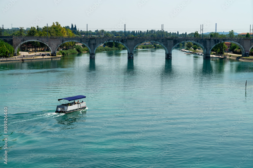 The tourist boat and the railway bridge over the Mincio river near Peschiera del Garda, Lago di Garda, Italy The tourist boat and the railway bridge over the Mincio river near Peschiera del Garda, Lago di Garda, Italy