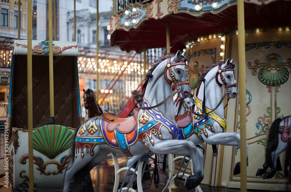 Horses with a carriage on a two-story city carousel against the backdrop of evening lights