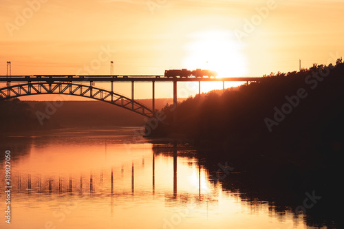 silhouette of the railway bridge over the river, a train is moving along it, the setting sun is shining