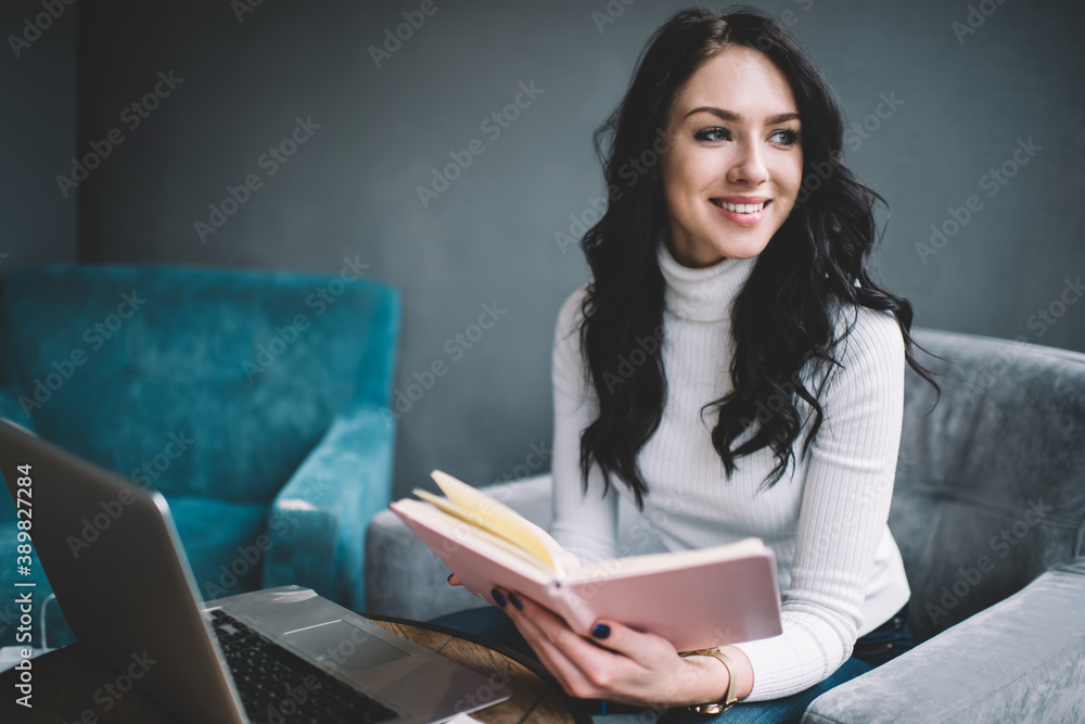 Trendy young woman chilling in armchair with book and laptop nearby Trendy young woman chilling in armchair with book and laptop nearby