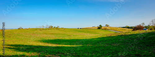 Panoramic hilltop meadow landscape with long shadow and blue sky in autumn