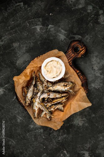 fried vendace with sauce, national Karelian dish, fried fish from Karelia, northern Russian cuisine, fried smelt, on a wooden tray, on a dark background
