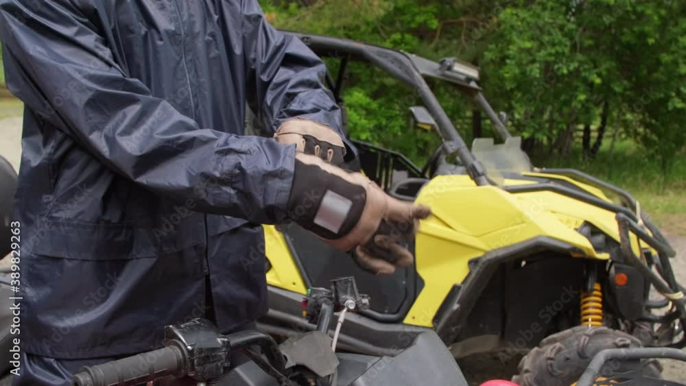 Tracking shot of middle-aged man with beard putting on riding gloves and sitting down on quad bike outdoors Tracking shot of middle-aged man with beard putting on riding gloves and sitting down on quad bike outdoors