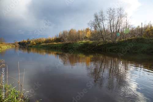 Landscape with trees in golden foliage reflecting in the river on a sunny autumn day.