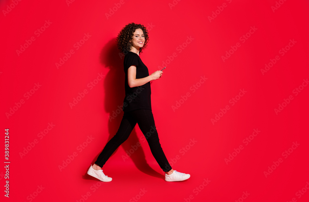 Full body profile side photo of brunette hair girl go empty space hold cellphone isolated over red color background Full body profile side photo of brunette hair girl go empty space hold cellphone isolated over red color background