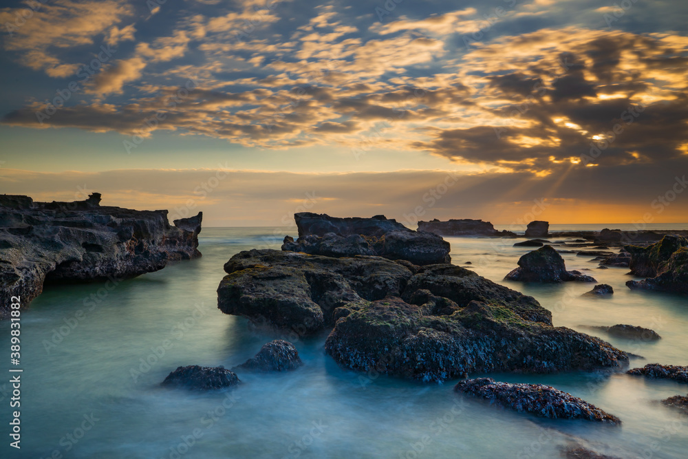 Beautiful seascape. Long exposure rocky beach during low ride. Panoramic ocean view. Composition of nature. Sunset scenery background. Cloudy sky. Water reflection. Mengening beach, Bali