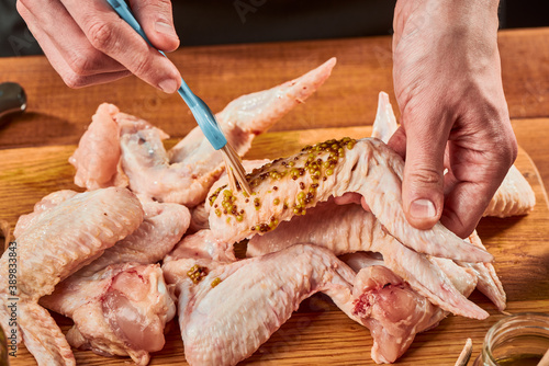 Man brushing raw chicken wings with French mustard