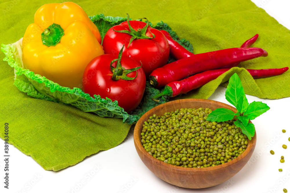 Mung bean (Vigna radiata) seeds in wooden bowl. fresh yellow paprika pepper, tomatoes, red chili pepper, savoy cabbage on tablecloth isolated on white background. Organic, healthy food concept Mung bean (Vigna radiata) seeds in wooden bowl. fresh yellow paprika pepper, tomatoes, red chili pepper, savoy cabbage on tablecloth isolated on white background. Organic, healthy food concept