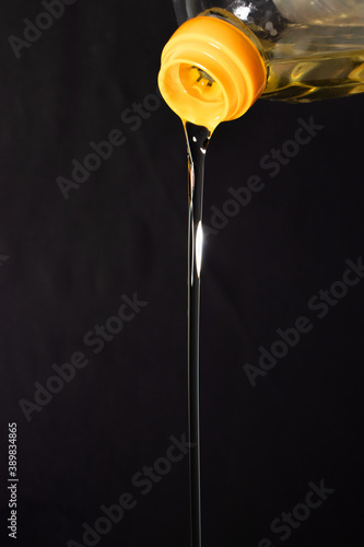 Pouring olive oil from a bottle on darck background photo