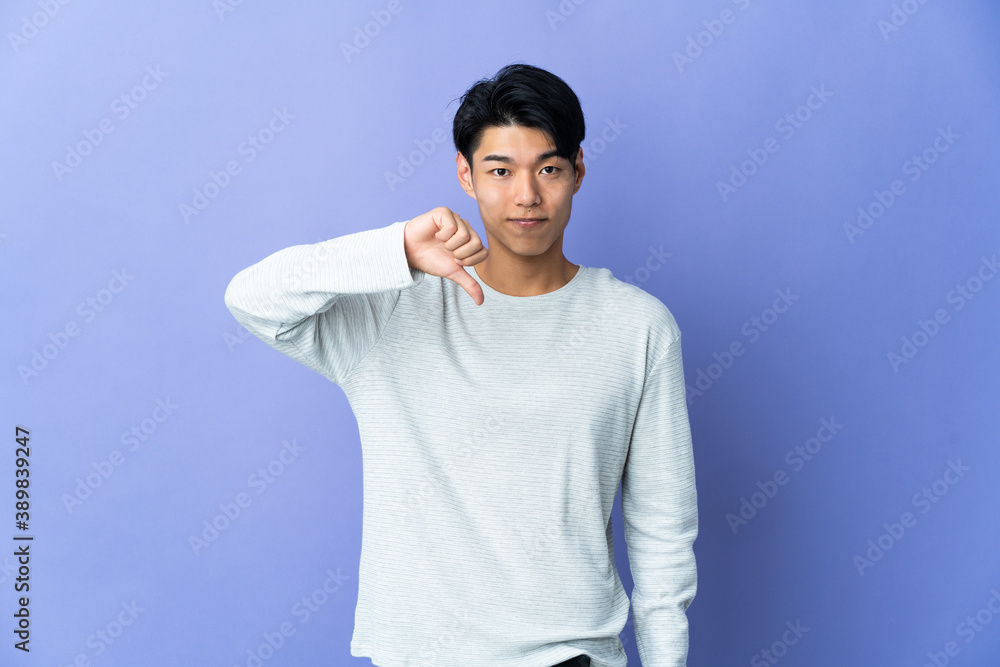 Young Chinese man isolated on purple background showing thumb down with negative expression Young Chinese man isolated on purple background showing thumb down with negative expression