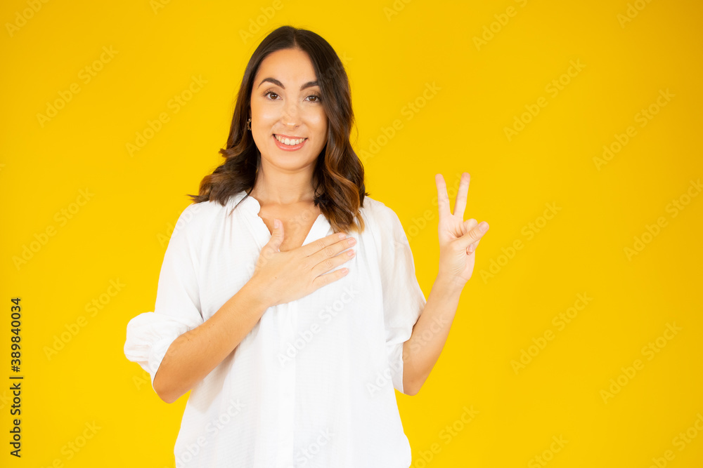Portrait of a smiling woman showing victory sign and looking at camera isolated on the yellow background Portrait of a smiling woman showing victory sign and looking at camera isolated on the yellow background