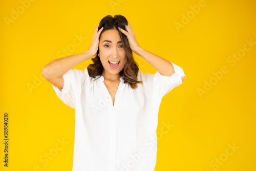 Beautiful young woman surprise holds head by hand. Shocked beautiful woman. Isolated on yellow background