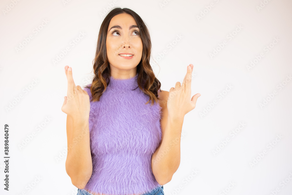 Portrait of a smiling young woman with brunette hair standing over white background, holding fingers crossed for good luck Portrait of a smiling young woman with brunette hair standing over white background, holding fingers crossed for good luck