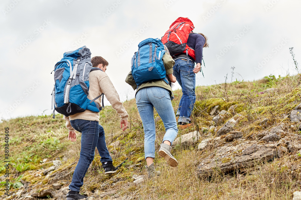 adventure, travel, tourism, hike and people concept - group of friends with backpacks climbing on hill