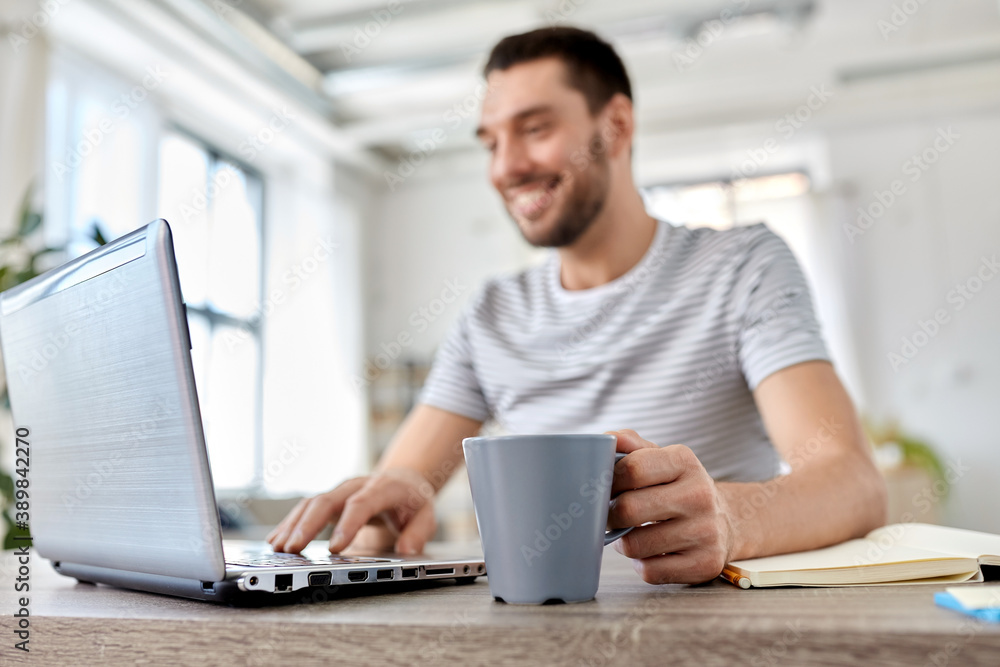technology, remote job and lifestyle concept - happy smiling man with laptop computer drinking coffee at home office technology, remote job and lifestyle concept - happy smiling man with laptop computer drinking coffee at home office