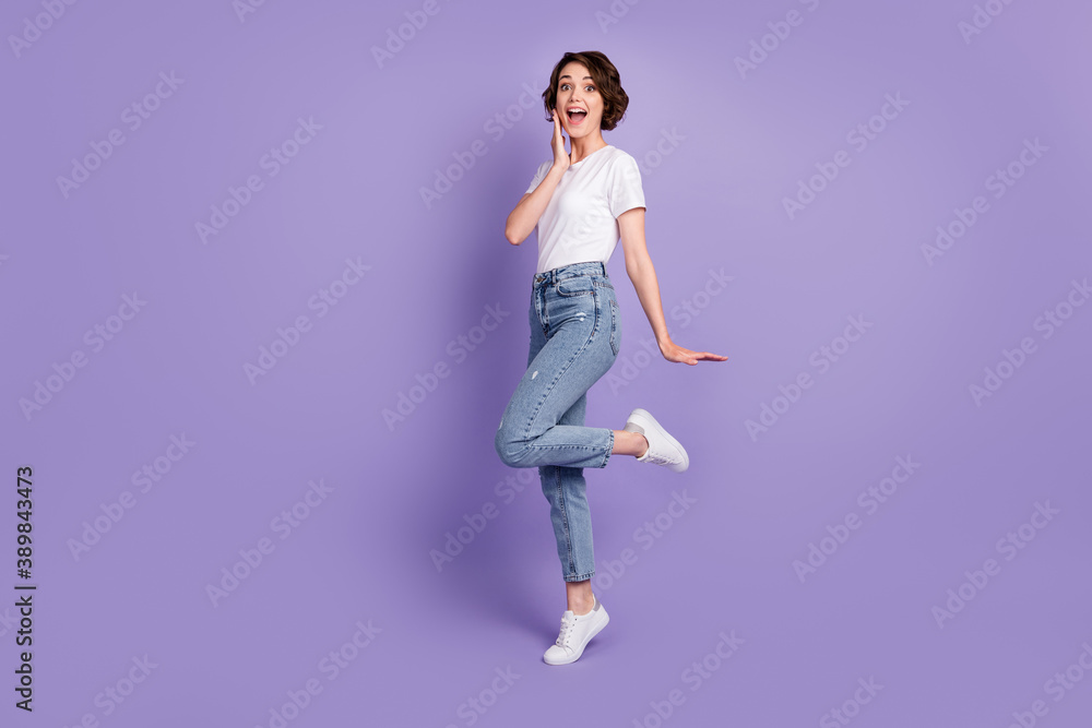 Photo portrait full length of adorable girl with open mouth touching face cheek with hand standing on one leg isolated on vivid purple colored background Photo portrait full length of adorable girl with open mouth touching face cheek with hand standing on one leg isolated on vivid purple colored background