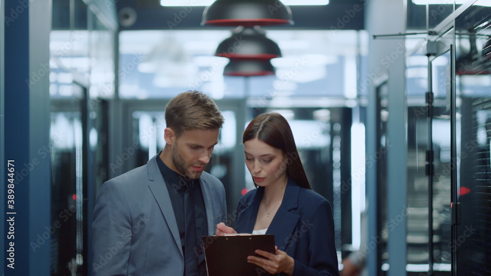 Young colleagues discussing project in corridor. Man and woman looking at charts Young colleagues discussing project in corridor. Man and woman looking at charts