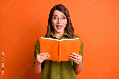 Photo portrait of surprised brunette girl keeping book laughing isolated on vivid orange color background