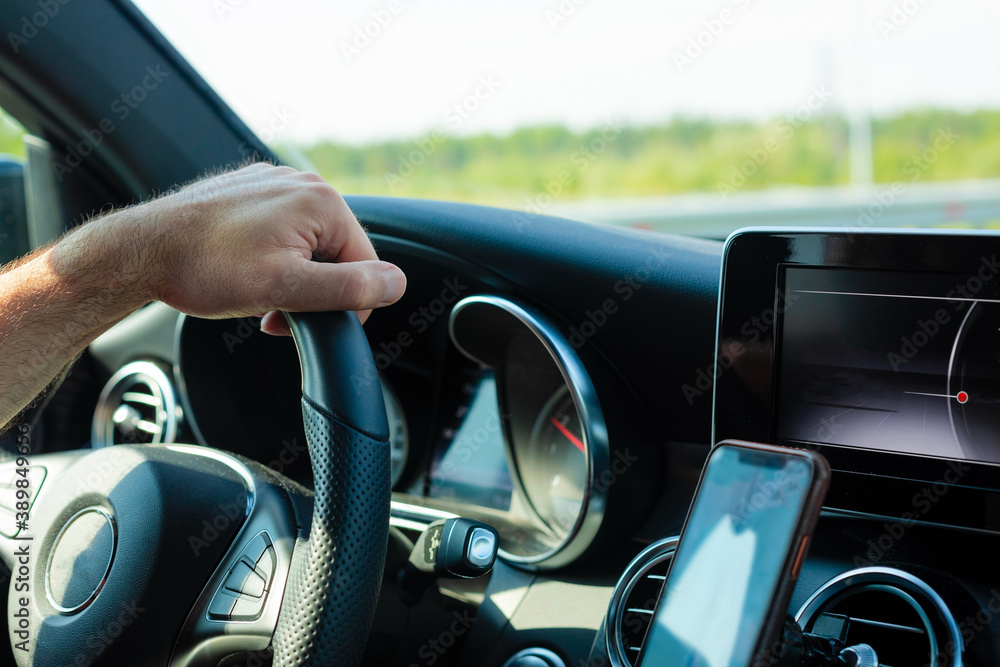 A man's brutal hand on the steering wheel of a car against the background of trees behind the windshield. The concept of freedom, traveling by car.