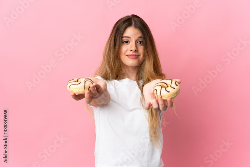 Young blonde woman isolated on pink background holding a donut and sad