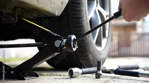Changing car wheel or tire. Man using car jack to unscrew and change wheel. Summer or winter tire swap in the backyard.