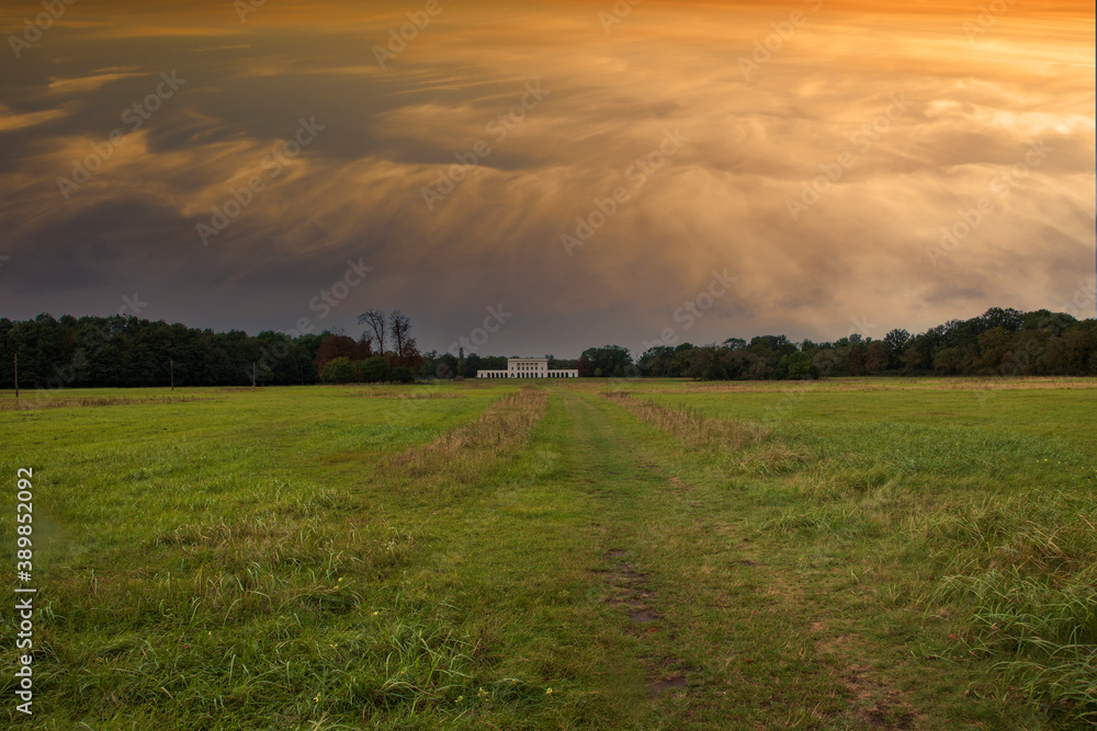 Large grassy meadow with Pohansko. There is a dramatic sky in the sky at sunrise.
